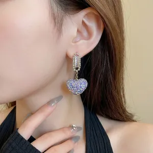 Boucles d'oreilles pendantes en cœur avec cristaux violets sur un modèle.