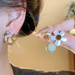 Detailed view of silver needle beaded circular studs and a white flower dangle earring