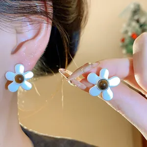 Detailed macro view of white flower stud earrings with brown center beads on ear