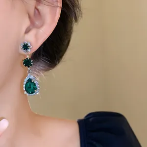Close-up view of elegant green emerald teardrop earrings with halo diamond accent