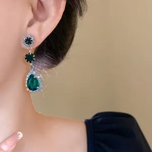 Close-up of emerald green teardrop dangling earrings with rhinestone accents on model.