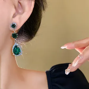 Close-up of emerald green water drop earrings with dazzling rhinestones on a model.