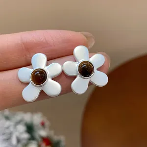 Vintage silver flower stud earrings with brown amber center stones shown on fingers