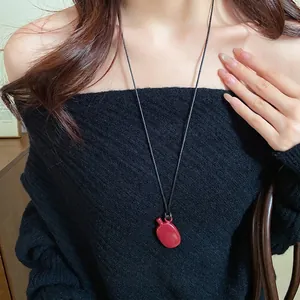 Vintage red water bottle pendant necklace with black cord on black knit sweater