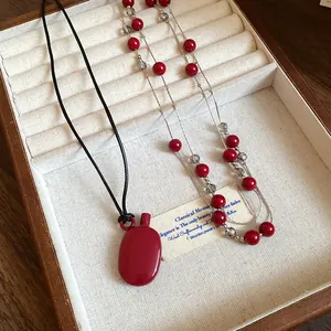 Detail view of retro red canteen pendant necklace and elegant beaded strand in jewelry tray.