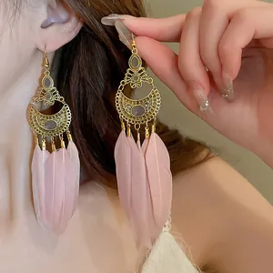 Pendientes largos boho vintage dorados con plumas rosas lucidos por una modelo