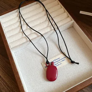Close-up of a vintage red bottle pendant on a black leather cord in a wooden box