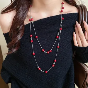 Detailed view of a long layered red bead necklace worn over a stylish black sweater