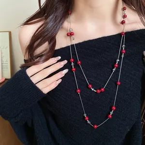 Detail shot of a long double-layered necklace with vibrant red beads on a black sweater.