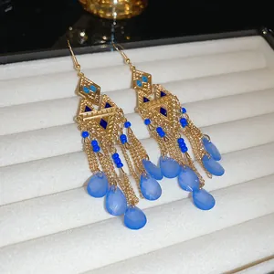 Primer plano de pendientes boho dorados con borlas y colgantes de hojas azules retro