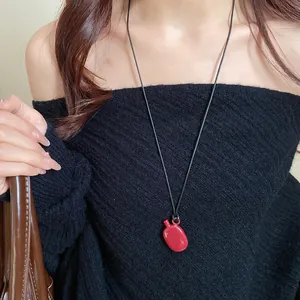 Detail showing a stylish red kettle pendant necklace on a black leather cord worn by a model