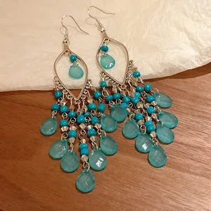 Vista detallada de pendientes bohemios con borlas, cuentas azules y gotas translúcidas.