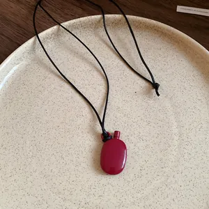 Detailed view of a dark red canteen-shaped pendant on a black minimalist cord necklace