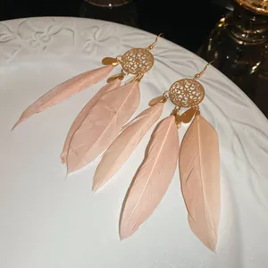Detailed view of bohemian long feather earrings with golden filigree disk design