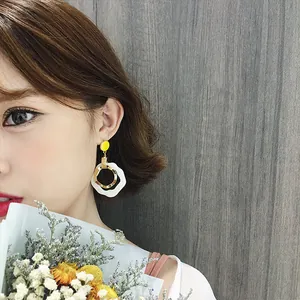 Model wearing elegant geometric drop earrings with yellow and white resin accents
