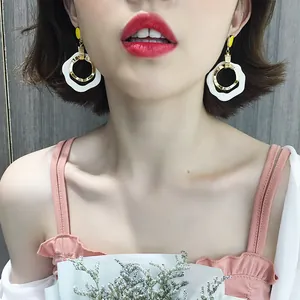 Close-up detail of white wavy hoop earrings with gold inner rings worn by an Asian model