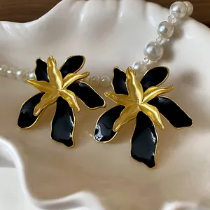 Detailed view of vintage black enamel and gold flower earrings inside a shell bowl