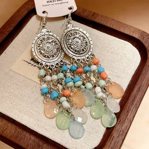 Detalle de pendientes largos bohemios con cuentas de colores y discos de plata vintage.