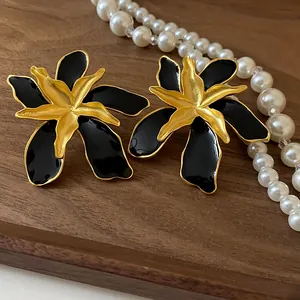 Close-up of vintage gold and black enamel flower stud earrings on a wood background.