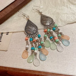 Detalle de pendientes bohemios con cuentas de colores y colgantes en forma de gota mate.