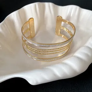 Close-up of a gold multi-layer open cuff bracelet with glitter and textured bands