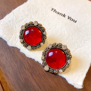 Primo piano di orecchini vintage in resina con pietra rossa e bordi dorati stile palazzo.