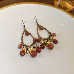 Primer plano detallado de pendientes bohemios vintage con cuentas de mármol rojo y dijes.