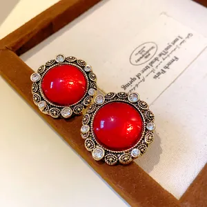 Dettaglio di orecchini vintage a bottone in resina rossa con elegante bordo di strass.