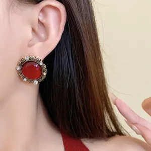 Primo piano di orecchini vintage in resina rossa con bordo dorato sull'orecchio modella.