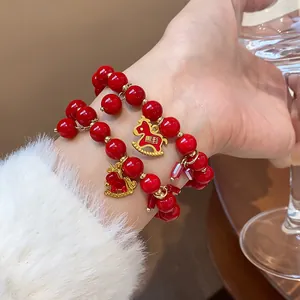 Detailed close-up view of red bead bracelet with gold rocking horse charm on female wrist.