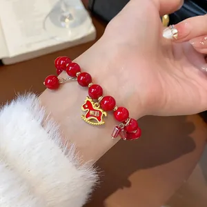 Elegant red beaded bracelet with gold rocking horse charm shown on a woman's wrist