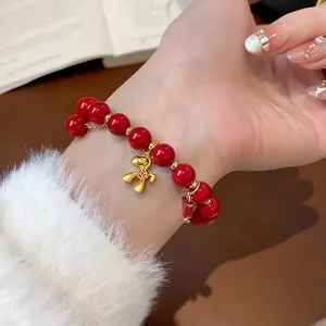 Detailed view of a red beaded bracelet featuring a golden horse charm on a female wrist.