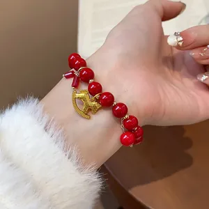 Detailed close-up of a red beaded bracelet with a golden rocking horse charm on a woman's wrist