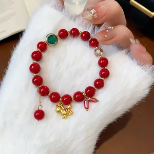 Macro detail of elegant red beaded bracelet featuring a golden horse charm and green stone