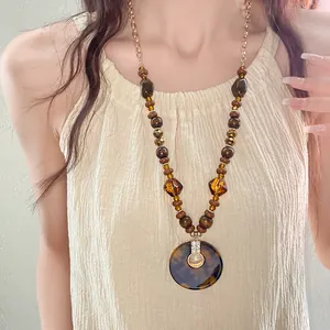 Detail of vintage ethnic necklace with wooden beads and round tortoiseshell pendant on model