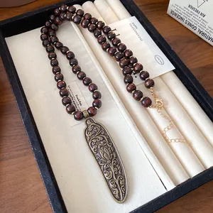 Close-up of vintage wood bead necklace with intricate bronze floral pendant in a jewelry box.