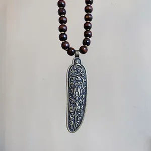 Detail of a vintage ethnic necklace featuring a carved metal pendant and dark wooden beads.