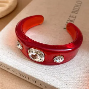 Close-up detail of a red resin cuff bracelet with three large embedded rhinestones