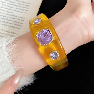 Close-up of yellow resin bangle with purple faceted stones and rhinestone detail.