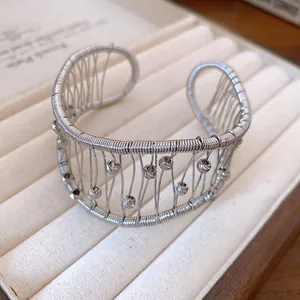 Close-up detail of silver woven wire cuff bracelet with textured beads and open design.