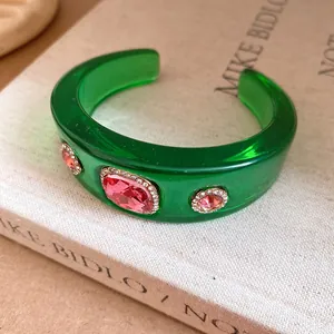 Close-up of a green resin cuff bracelet with pink rhinestone embellishments on a book