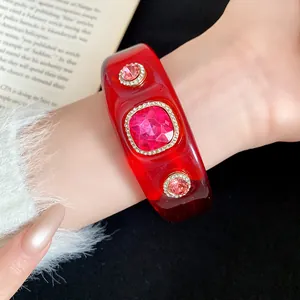 Detailed view of a bold red resin bangle with sparkling pink crystal inlays worn on a wrist.