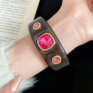 Close-up of a dark grey resin cuff bracelet featuring sparkling pink crystals and rhinestones