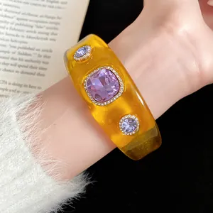 Detailed view of amber translucent resin bangle with purple crystal and rhinestones