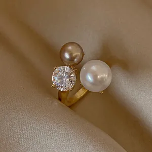 Primo piano di un elegante anello aperto dorato con due perle e una pietra di zircone