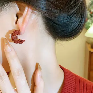 Dettaglio di un orecchino rosso a forma di C con fiori plissettati indossato