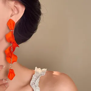 Asian model wearing vibrant orange bohemian petal tassel earrings with gold chain detail