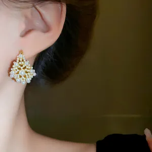 Close-up of elegant gold-plated cluster pearl earrings worn on a female model's ear.