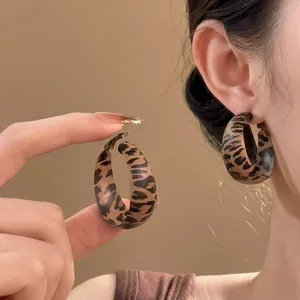 Detail of leopard print fabric hoop earring worn on ear with soft lighting.