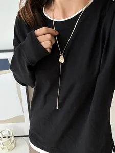 Detail of a gold-plated irregular pendant adjustable sweater necklace on black outfit.